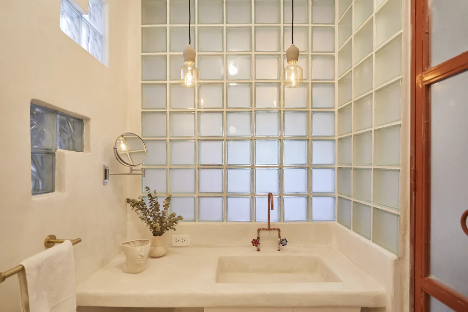 A broad vanity, glass blocks and a round mirror in JA1’s bathroom
