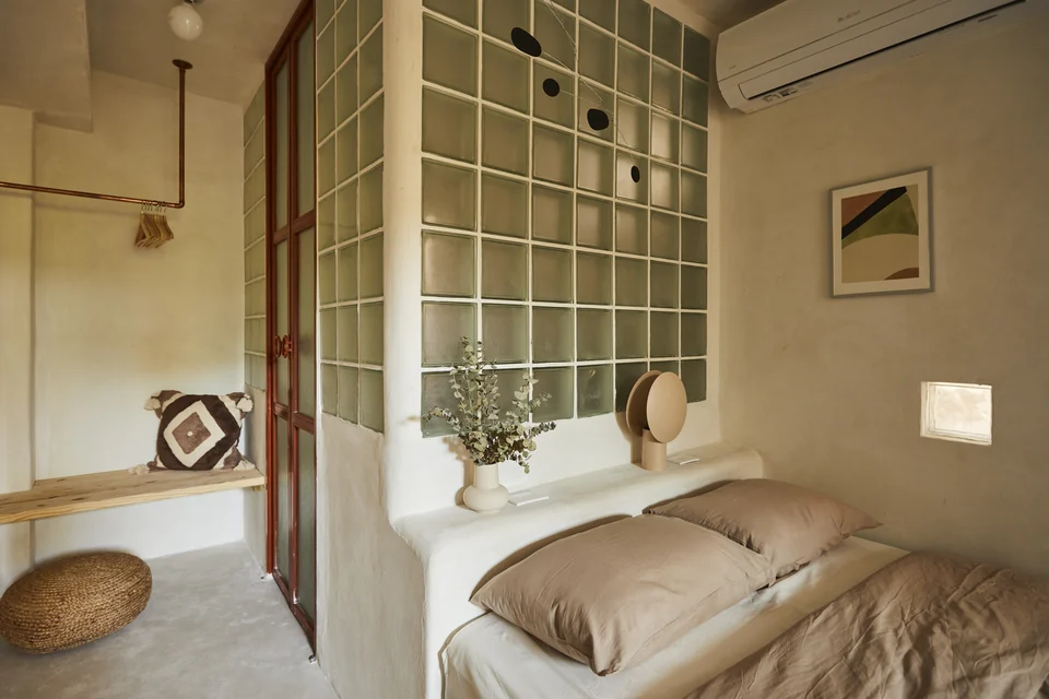JA1’s queen bed beside glass blocks and warm wood details