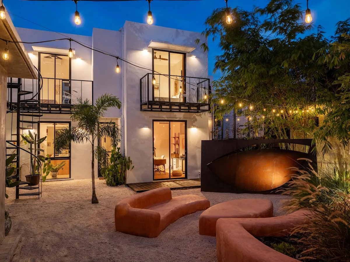 The courtyard at Casa Frida by DW at dusk, with string lights over the sculpted seating and the Dreamers Welcome house behind.