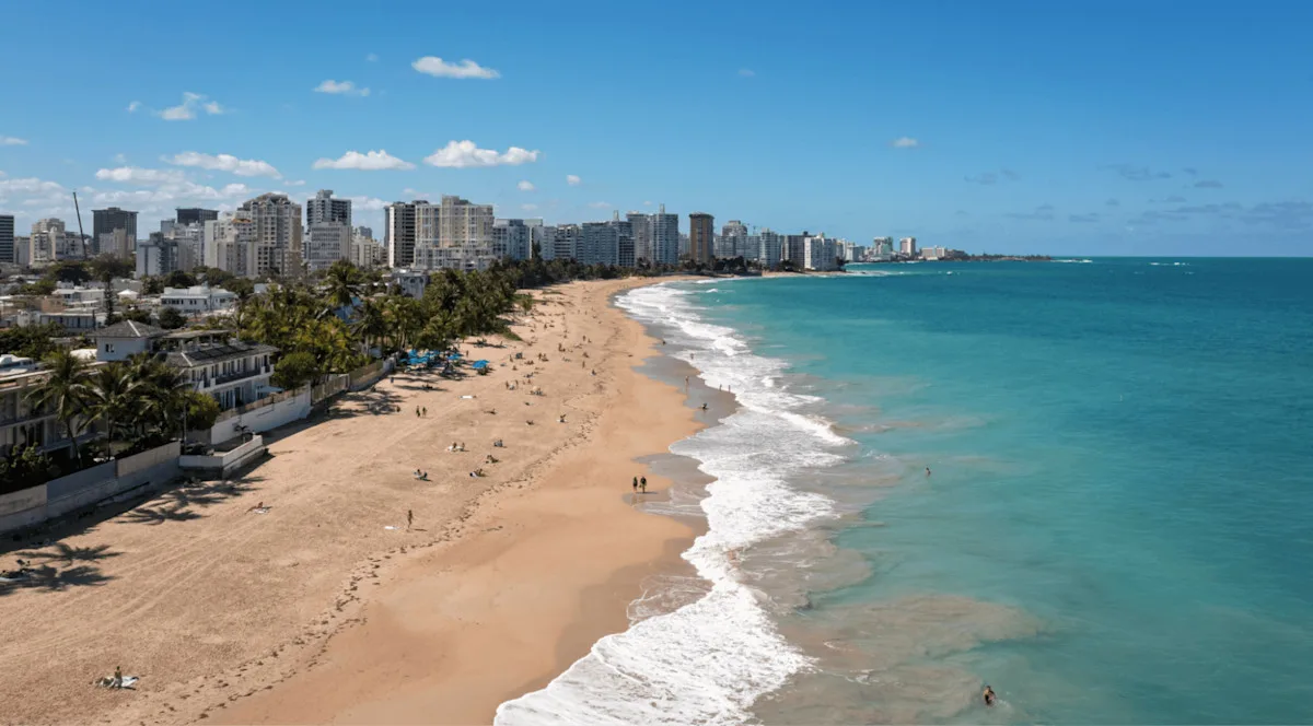 A San Juan beach seen from the air, with the high-rise hotels and apartment towers of the city's beach strip running behind the sand.
