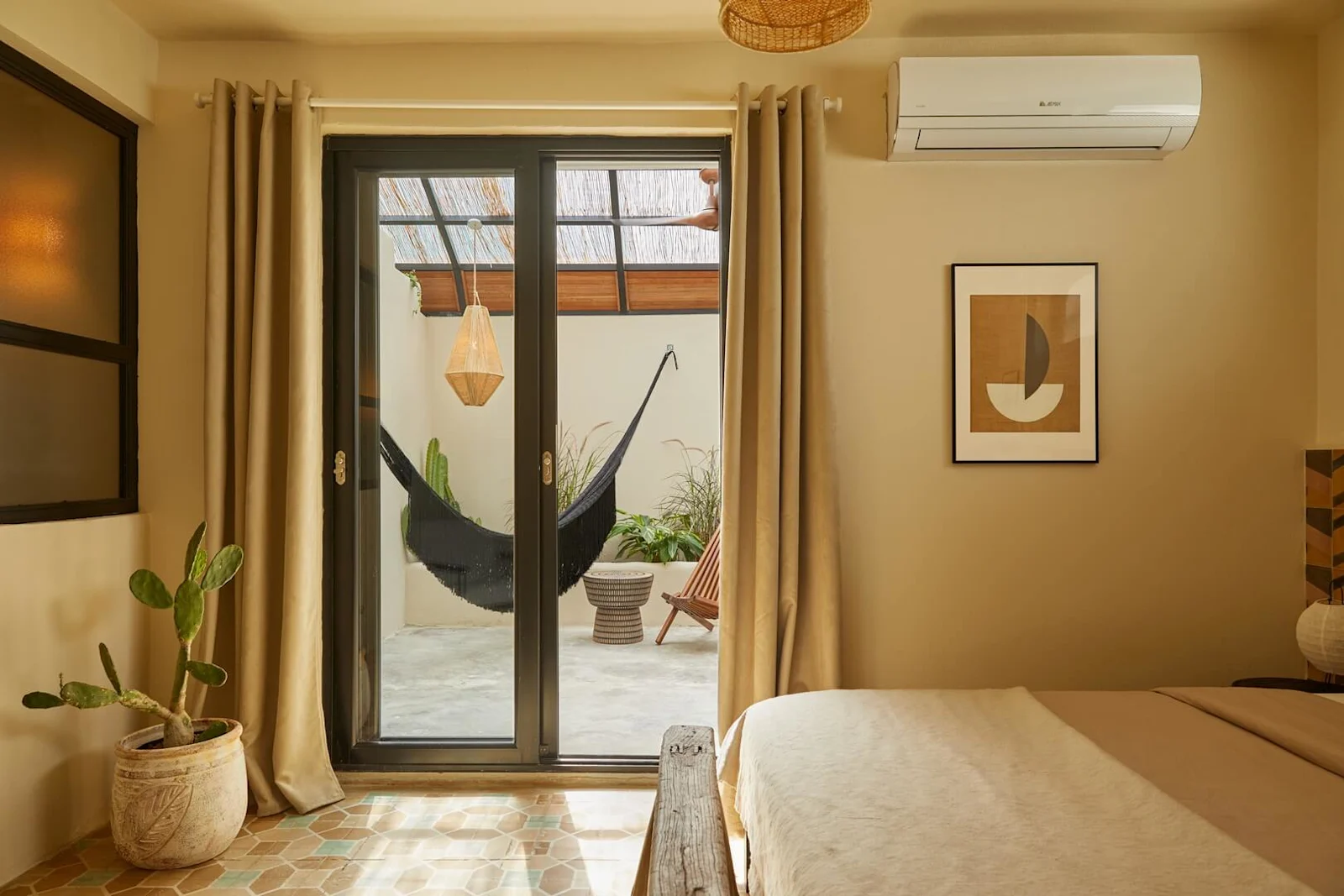 A cozy hotel room opening up through sliding glass doors to a private outdoor patio with a black hammock and potted cacti.