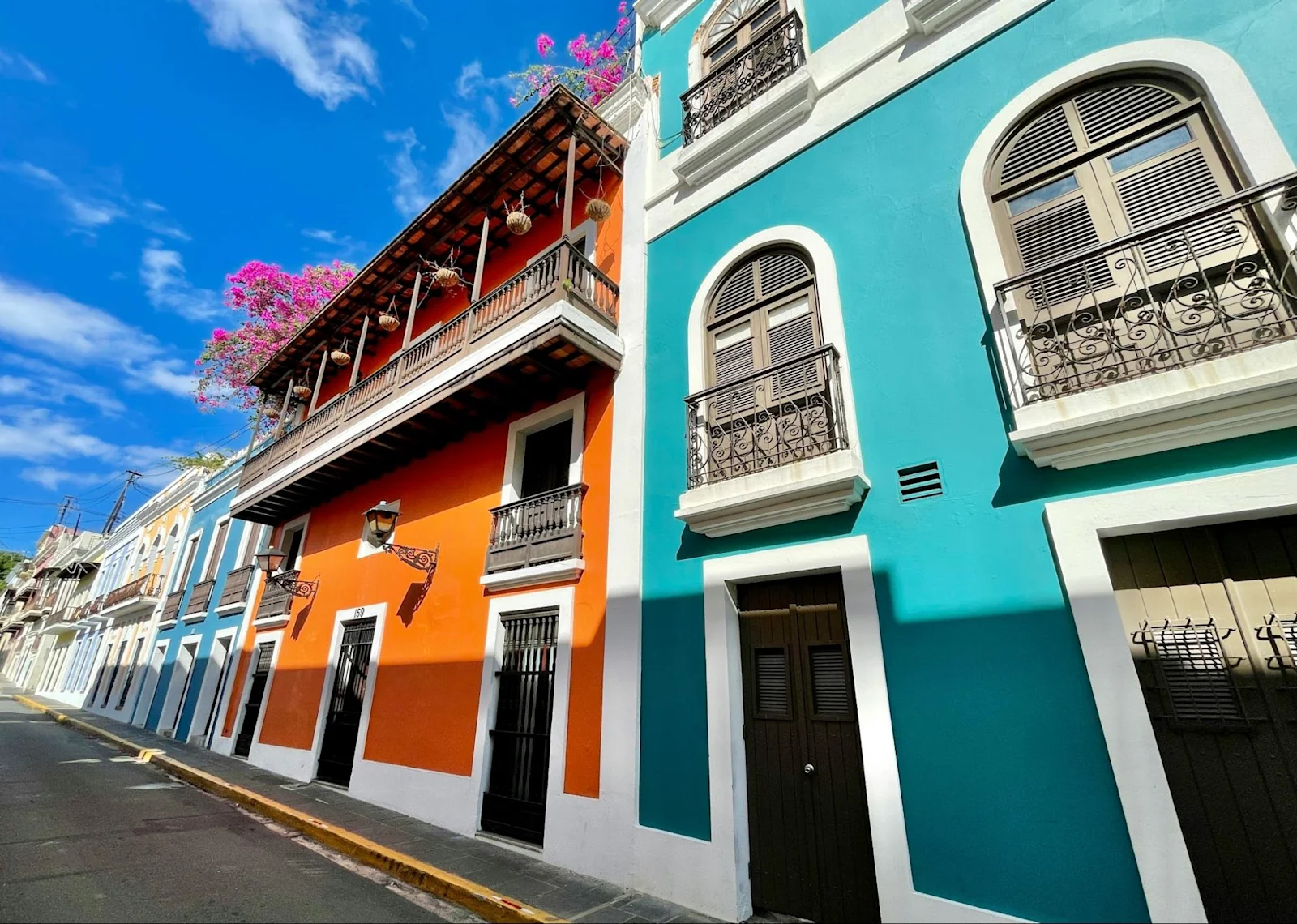 Brightly painted colonial houses in orange and turquoise along a street in Old San Juan.
