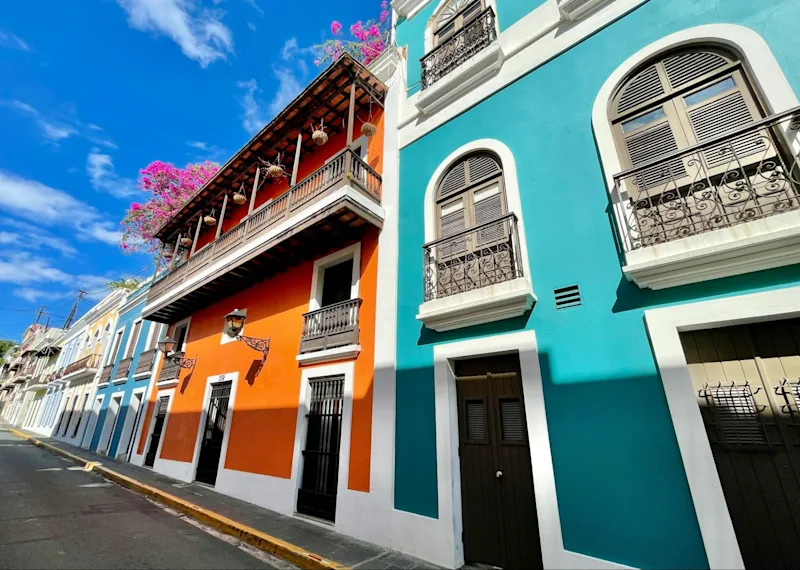 Brightly painted colonial houses in orange and turquoise along a street in Old San Juan.
