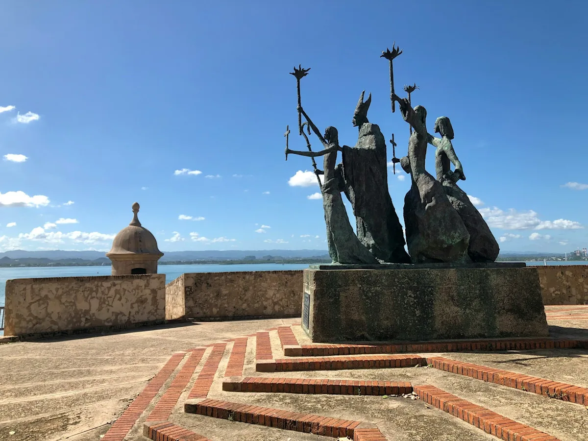 Bronze figures of the Raíces sculpture beside a stone sentry box on the old city walls of San Juan.