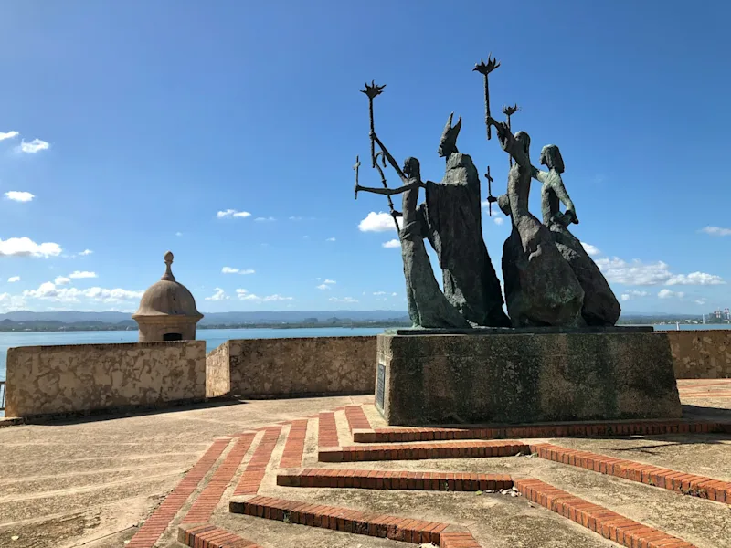 Bronze figures of the Raíces sculpture beside a stone sentry box on the old city walls of San Juan.