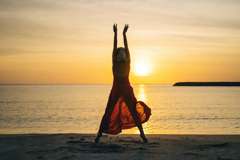 A silhouetted figure stretching on a beach as the sun sets over the sea.