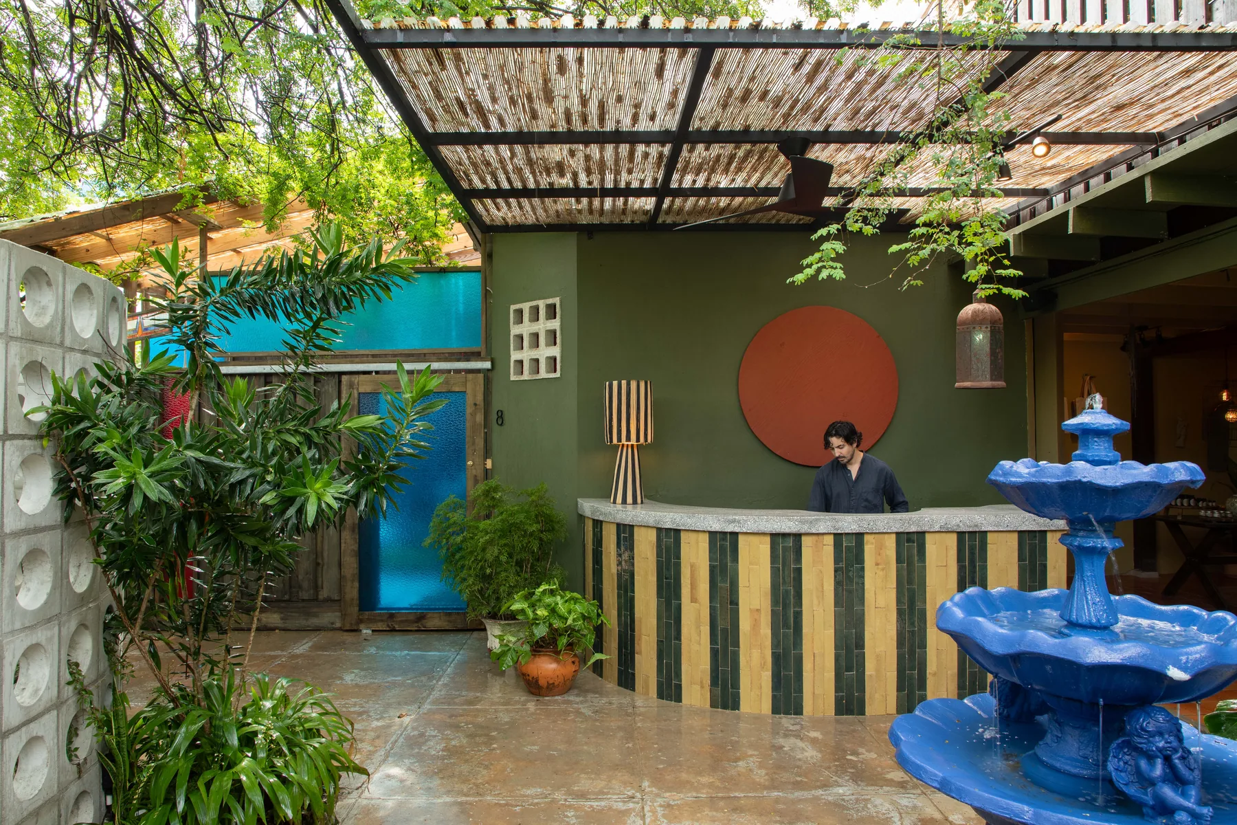 Tree-shaded reception courtyard with striped counter and blue fountain at Dreamcatcher