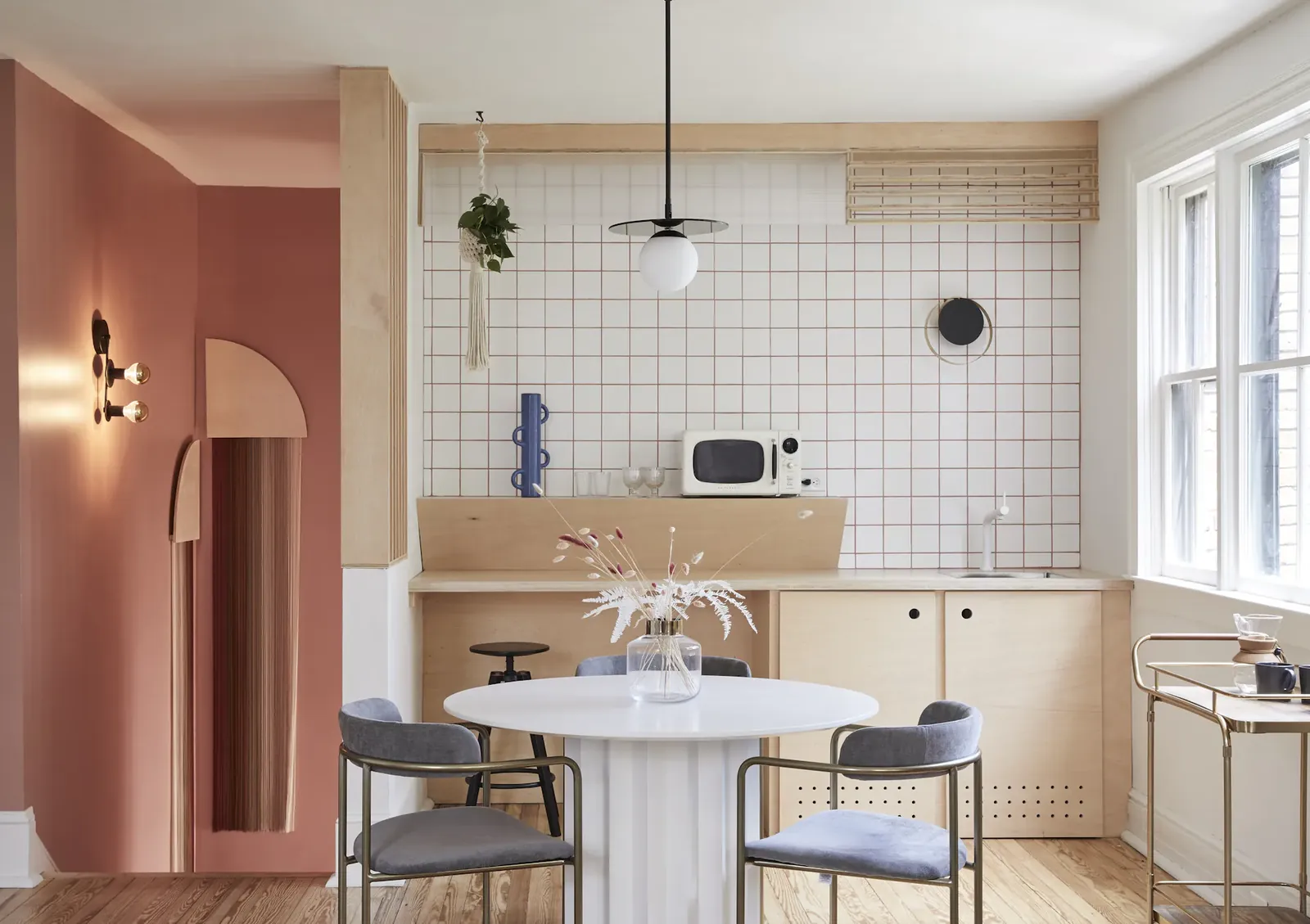A pink doorway beside a cream tiled kitchen and a round white dining table.