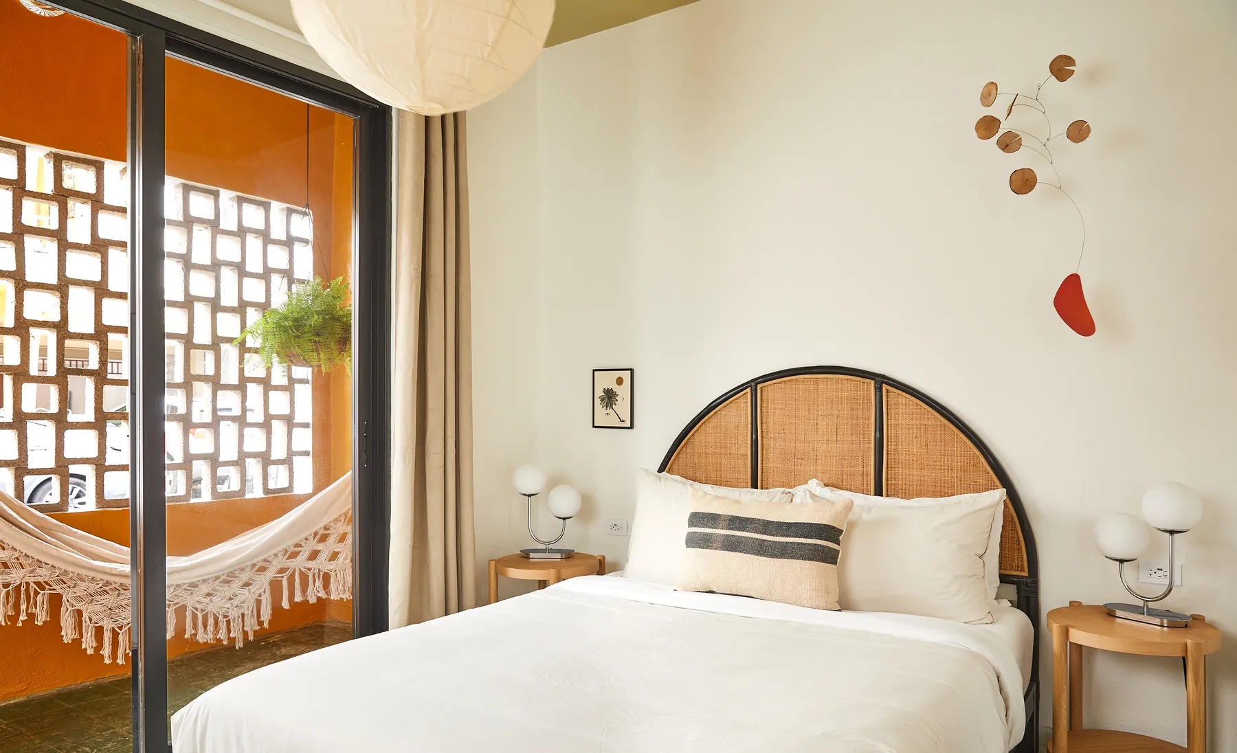 Woven headboard, white linen and an open balcony with a hammock in an APT bedroom.