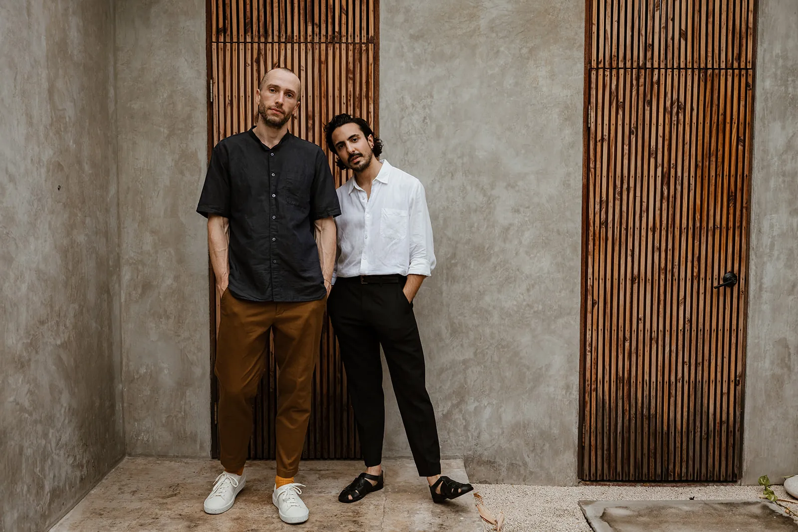 Dreamers Welcome founders Stephan Watts and Roy Delgado standing beside a concrete wall and timber screens.