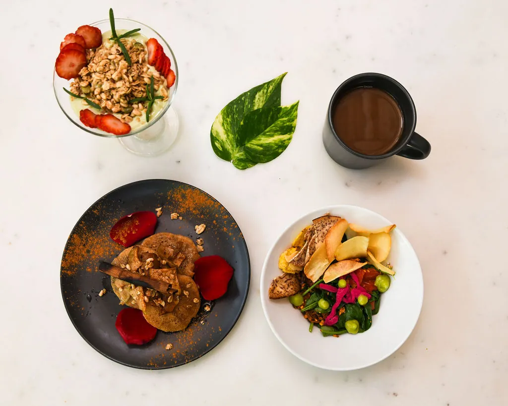 Colorful plant-based breakfast plates, coffee and fruit on a white tabletop at Dreamcatcher.