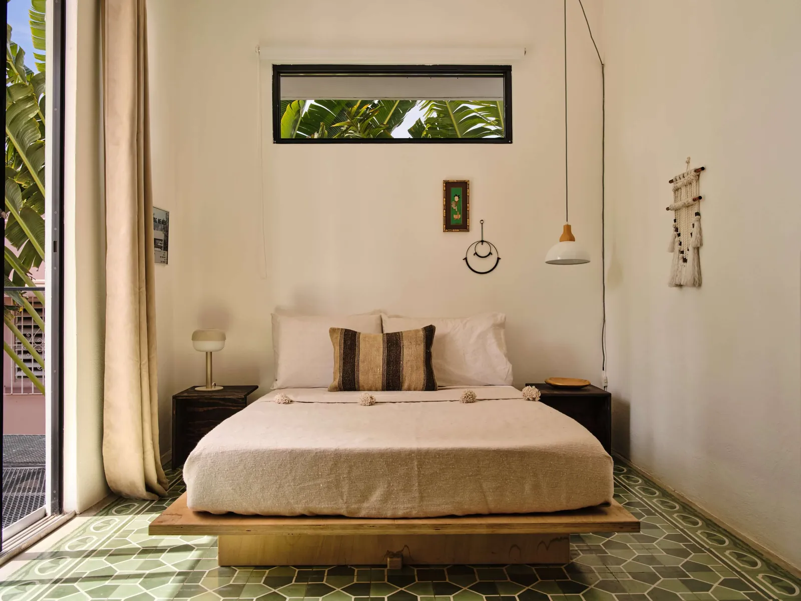 A low bed, patterned green floor and hanging details in a light-filled Casa Frida bedroom.