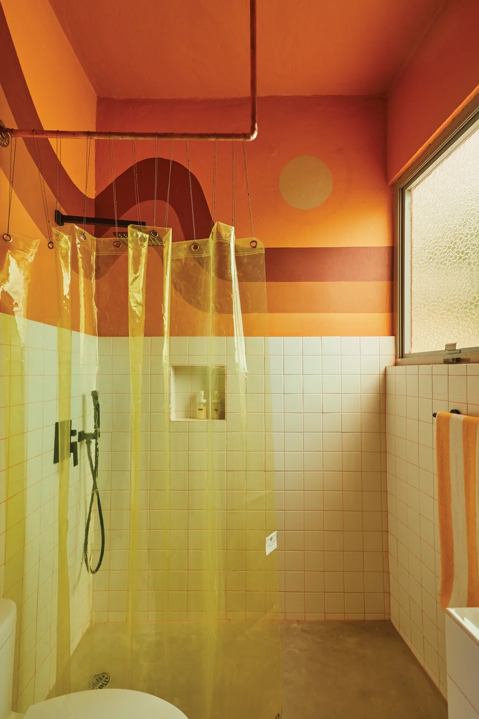 Orange and yellow walls with a translucent curtain around Diana’s rain shower