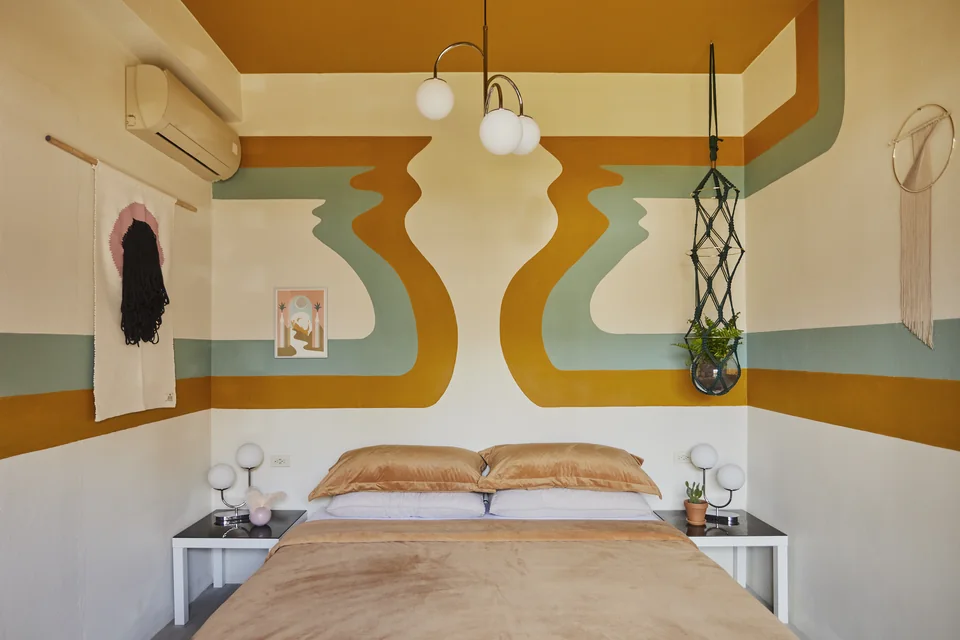 King bed beneath graphic green, gold and cream stripes in Gloria