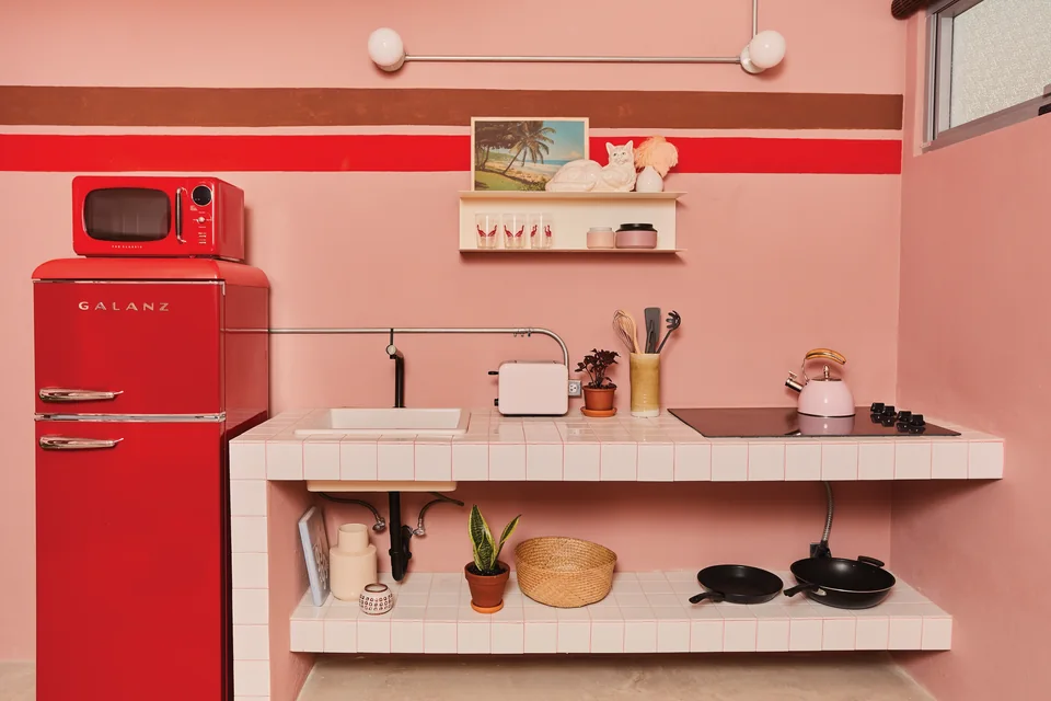 Red mini fridge, pink cabinetry and open shelving in Grace’s kitchenette