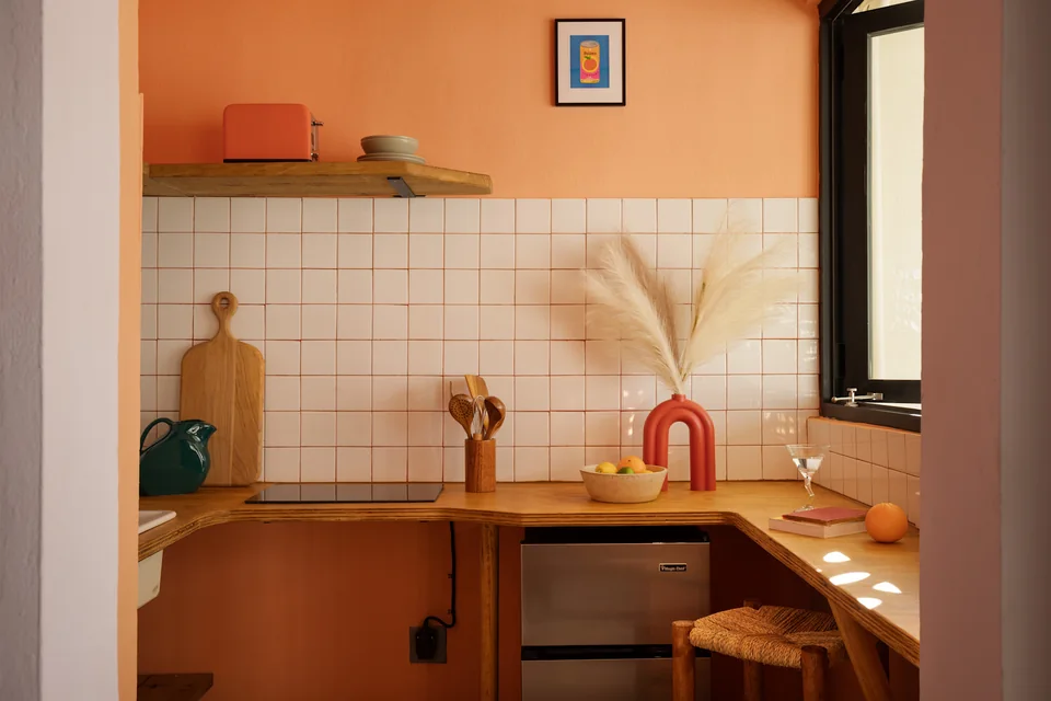 A’s orange kitchenette with timber cabinets and a pink tap