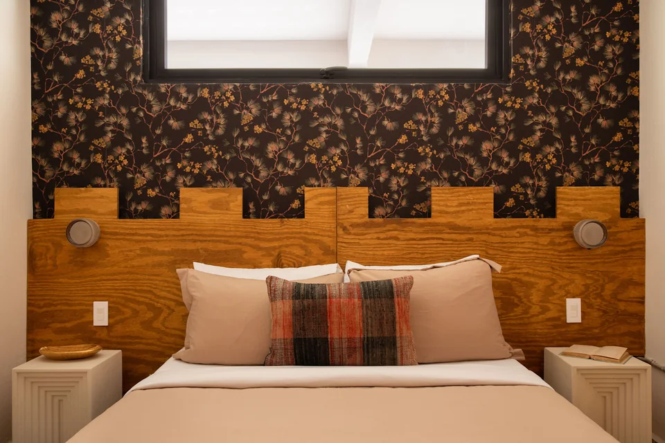 Queen bed with timber headboard and dark floral wallpaper in N