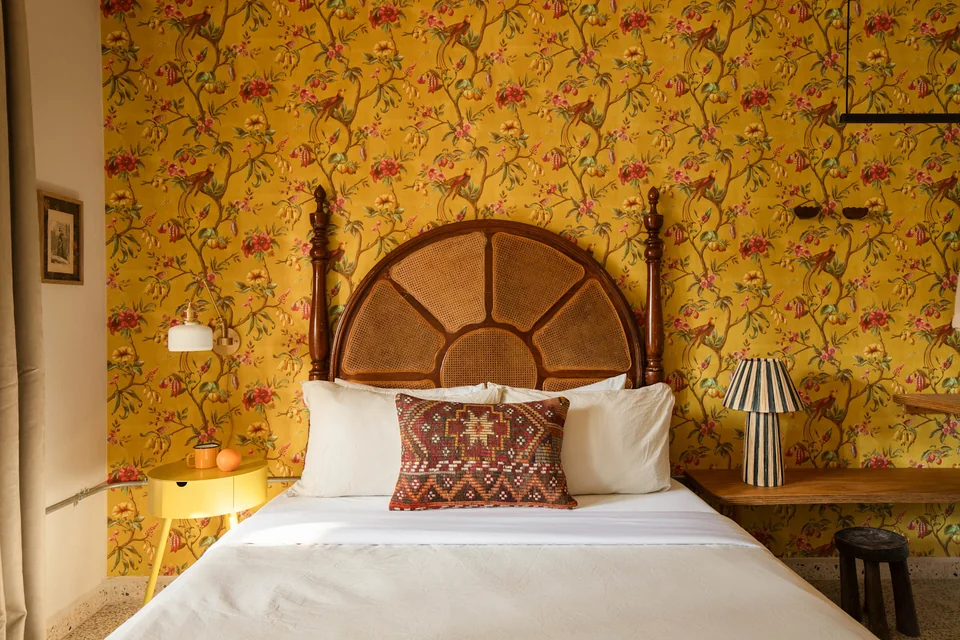 Queen bed and woven headboard framed by yellow floral wallpaper in O