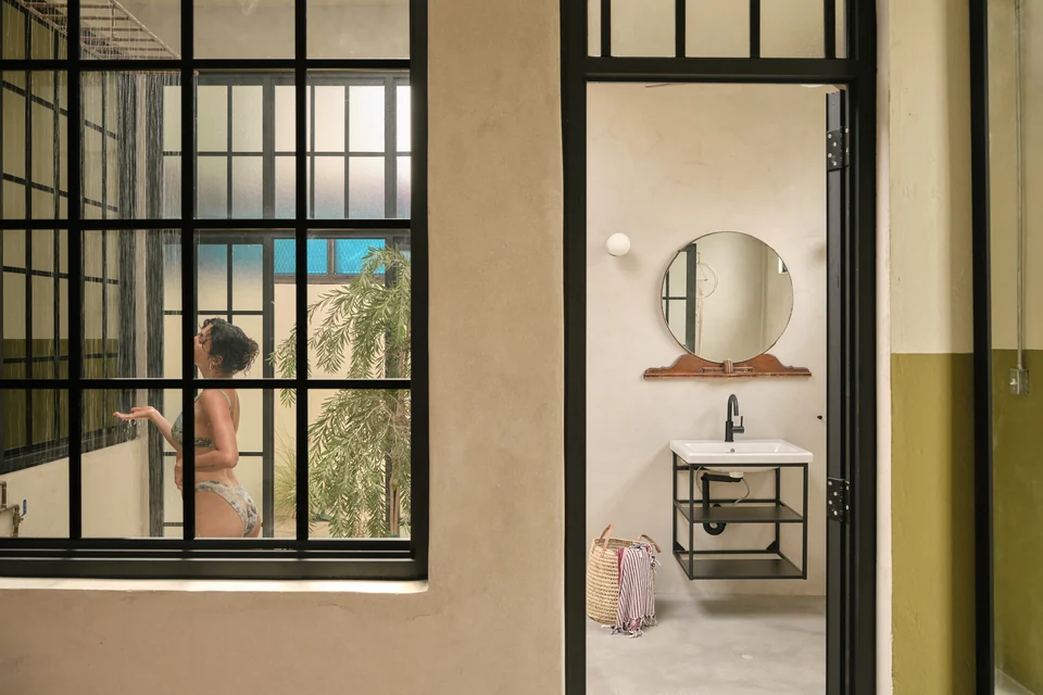 A round mirror and stone basin beside the black-paned windows in Paz 3’s bathroom