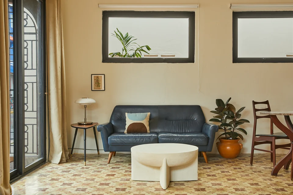 A blue loveseat, round coffee table and planted corner in Rosa 1
