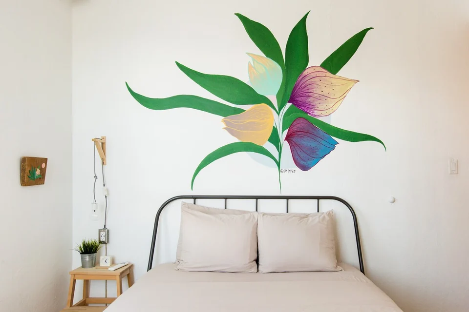 A queen bed and green bird mural in Adventurer’s first bedroom