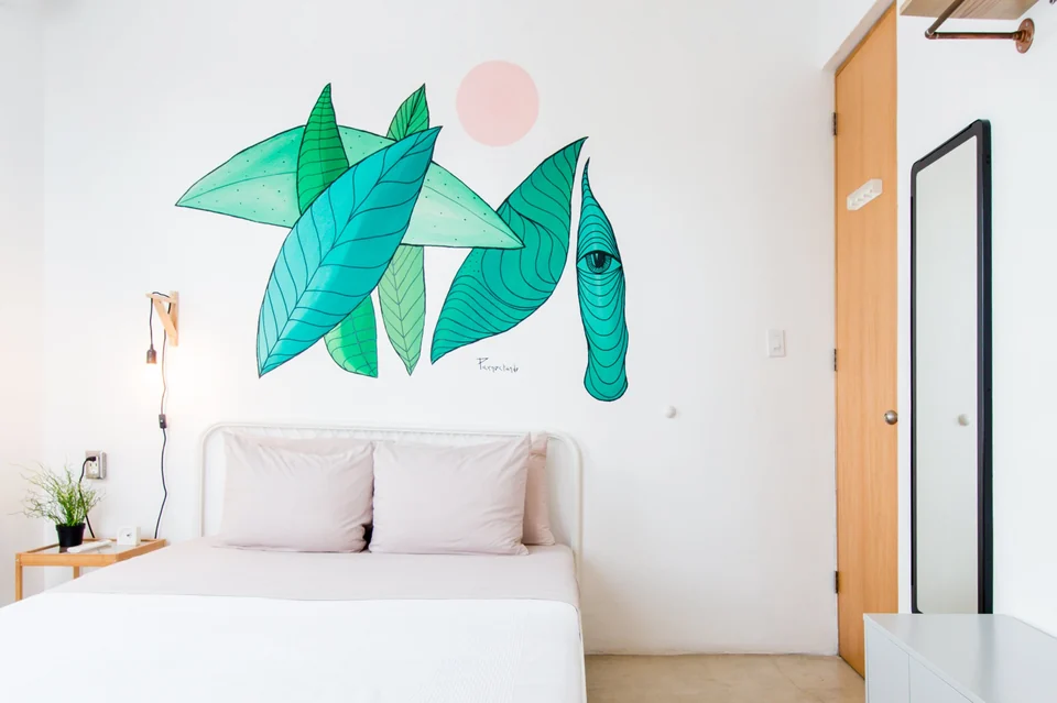 A queen bed and green tropical mural in Dreamer’s first bedroom
