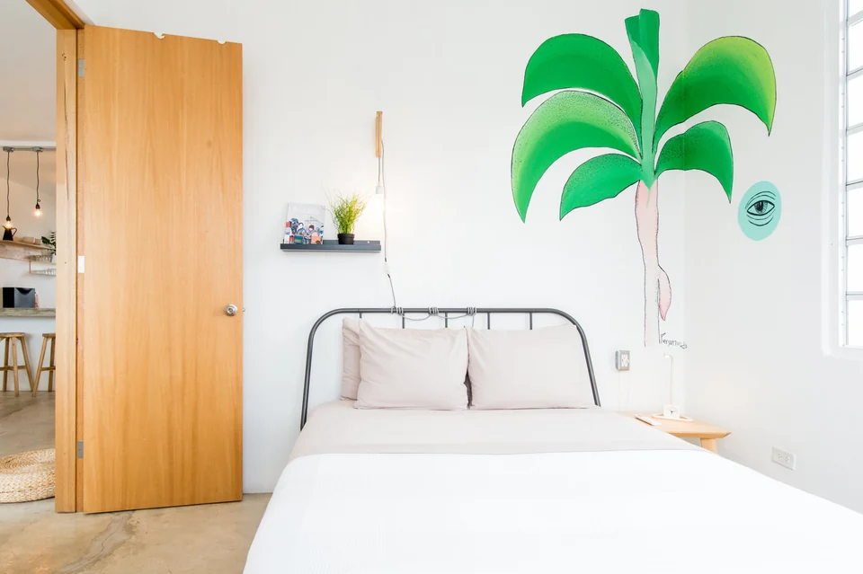 A queen bed beneath a green palm mural in Dreamer’s third bedroom