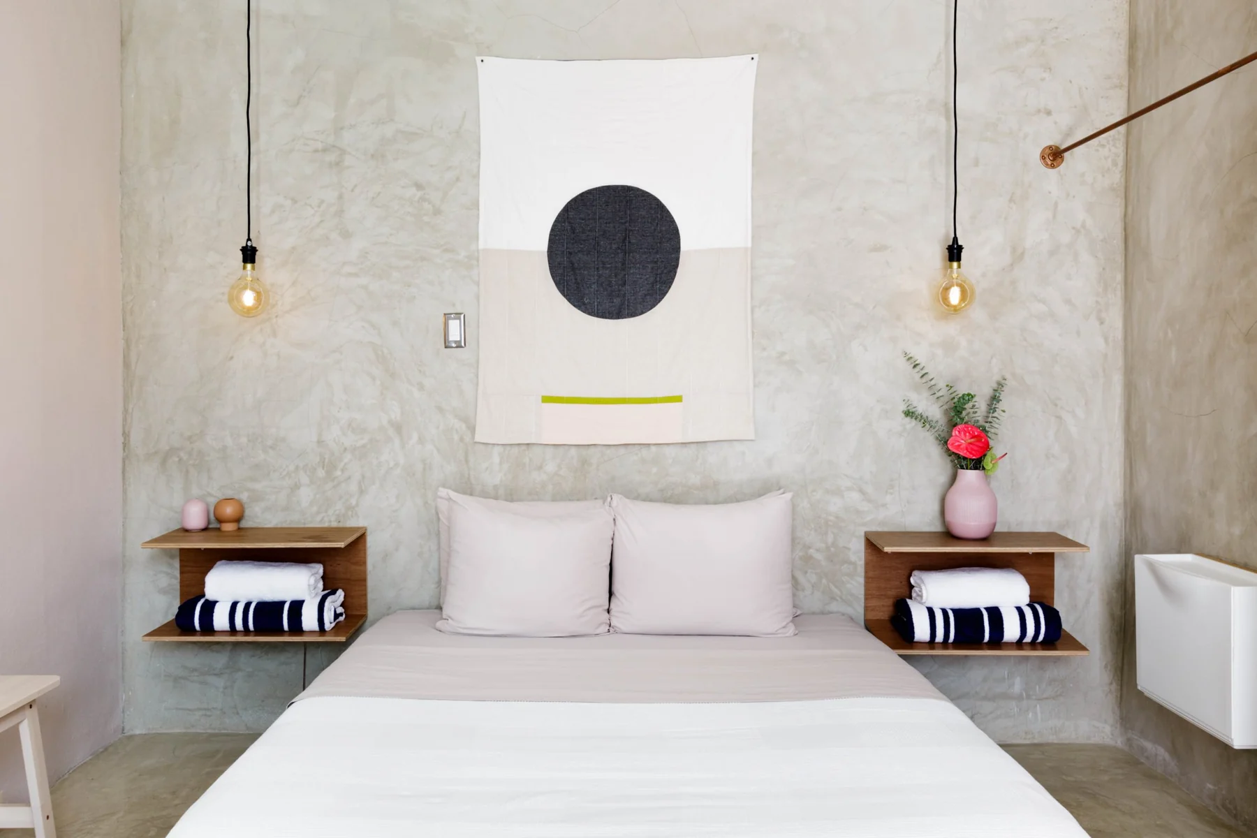 Lover’s queen bed, concrete wall, graphic artwork and woven pendant lights