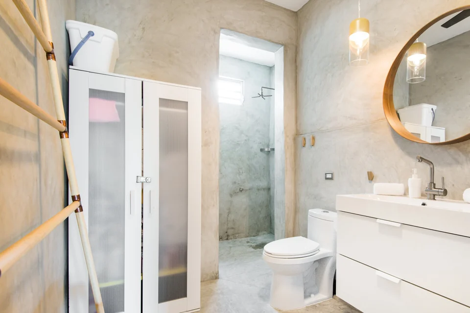 Nomad’s bathroom with a round mirror, glass shower and concrete walls